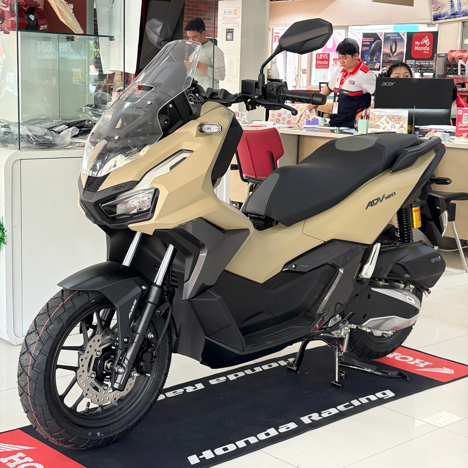 Honda ADV 160 สีทรายด้าน ถ่ายภาพจริงที่โชว์รูม Honda มุมด้านหน้าซ้าย เห็นโช้คหลังและยางกึ่งวิบากชัดเจน